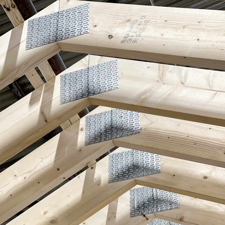 Sluoksniuotos medinės stogo santvarų dalys su įpresuotomis metalinėmis jungtimis gamybos ceche.